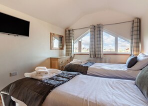 Un dormitorio con dos camas, un aparador, un televisor y un ventanal con cortinas.