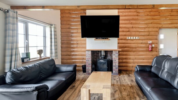 Una sala de estar con chimenea, dos sofás de cuero negro, una mesa de centro de madera y un televisor de pantalla plana montado en una pared de madera.