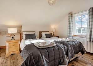 A bedroom with two beds, bedside tables, lamps, a radiator, and a window with curtains. - 5 bedroom accommodation in Hornsea (Hornsea)
