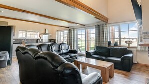 Amplia sala de estar con sofás de cuero, una mesa de centro de madera y grandes ventanales con vistas al exterior.