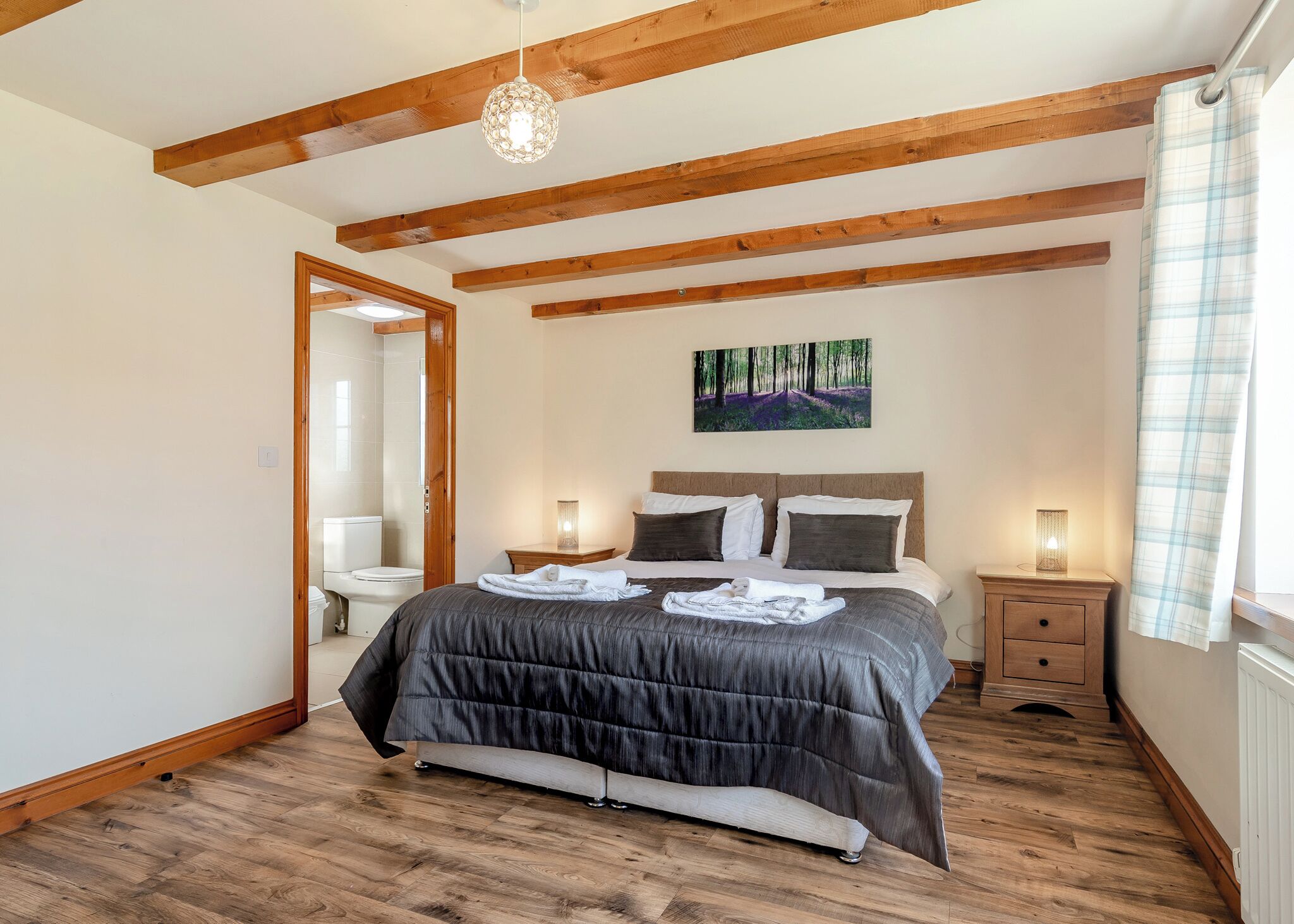 Une chambre à coucher avec un lit, des poutres en bois, un tableau, une table de chevet et une fenêtre avec un rideau.