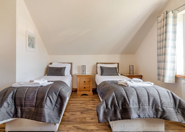 Une chambre avec deux lits, un plancher en bois et une fenêtre avec des rideaux.
