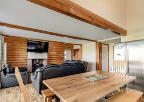 A wooden dining table with benches, a black leather sofa, a fireplace, and a television mounted on the wall.