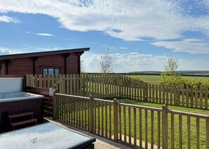 Une terrasse en bois avec un jacuzzi, une clôture en bois et une vue sur un champ verdoyant.