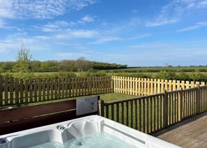 Ein Whirlpool auf einer Holzterrasse mit Blick auf einen eingezäunten Garten und die ferne Landschaft.