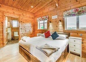 Une chambre à coucher située dans une cabane en bois, avec un lit, des tables de chevet, une fenêtre offrant une vue et une salle de bain visible à travers une porte ouverte.