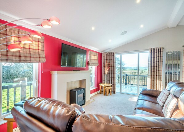 A living room with a fireplace, leather sofa, television, and a balcony with a view.