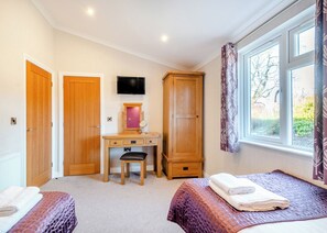 A bedroom with two beds, a desk with a chair, a wardrobe, a TV, and a window with curtains.