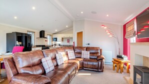 Ein modernes Wohnzimmer mit einer ledernen Eckcouch, einer Küche im Hintergrund und einem Kamin mit roter Akzentwand.