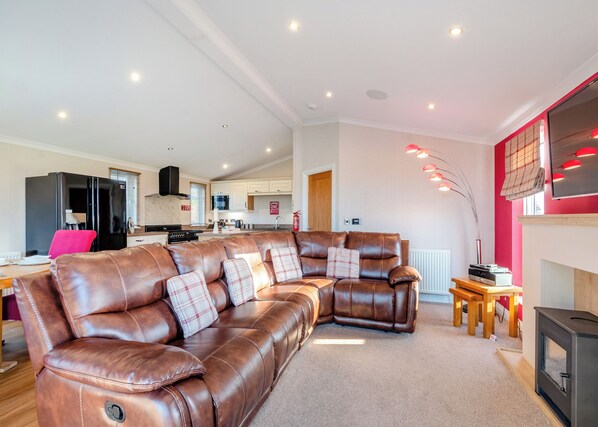 Un salon moderne avec un canapé d’angle en cuir, une cuisine en arrière-plan et une cheminée agrémentée d’un mur d’accent rouge.