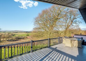 Une terrasse en bois offrant une vue sur un paysage rural, avec un arbre et des champs situés au loin.