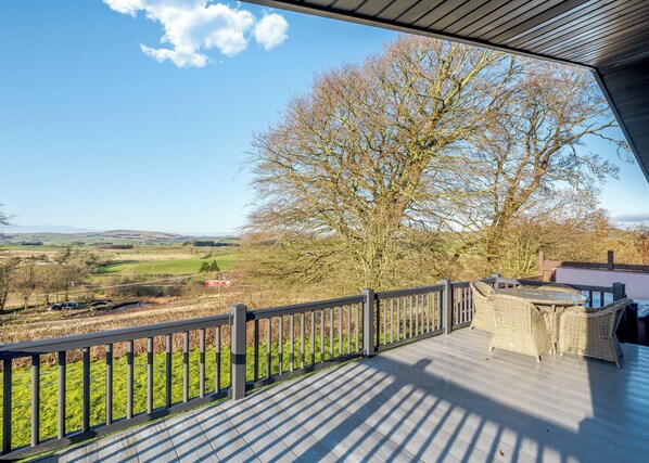 A wooden deck with a view of a rural landscape, including a tree and distant fields.