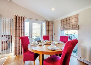 Un espace repas avec une table ronde, des chaises rouges et une vue dégagée sur l’extérieur grâce à de grandes fenêtres.