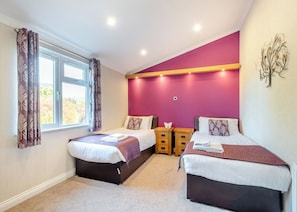 A bedroom with two beds, a window with curtains, a nightstand, and a wall-mounted decoration.