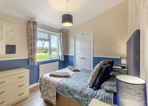 A bedroom with a bed, a bedside table, a lamp, a window with curtains, a radiator, and a door. - 2 bedroom accommodation in Swinethorpe, Nr Lincoln (Swinethorpe, Nr Lincoln)