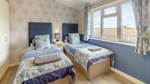 A bedroom with two single beds, a window with curtains, a hanging light fixture, and a patterned wallpaper. - 2 bedroom accommodation in Swinethorpe, Nr Lincoln (Swinethorpe, Nr Lincoln)