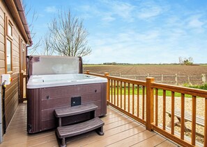 A hot tub on a wooden deck with a view of a field.