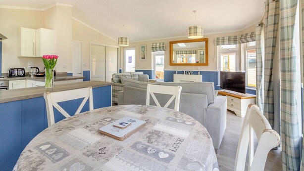 A modern kitchen with white cabinets, a dining table with a newspaper-patterned tablecloth, and a living area with a sofa and TV. - 2 bedroom accommodation in Swinethorpe, Nr Lincoln (Swinethorpe, Nr Lincoln)