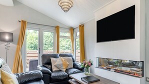 A modern living room with a leather sofa, a wooden coffee table, a flat-screen TV, and a fireplace. - Bakewell Deluxe Lodge Pet Friendly (Longnor, Nr. Buxton)