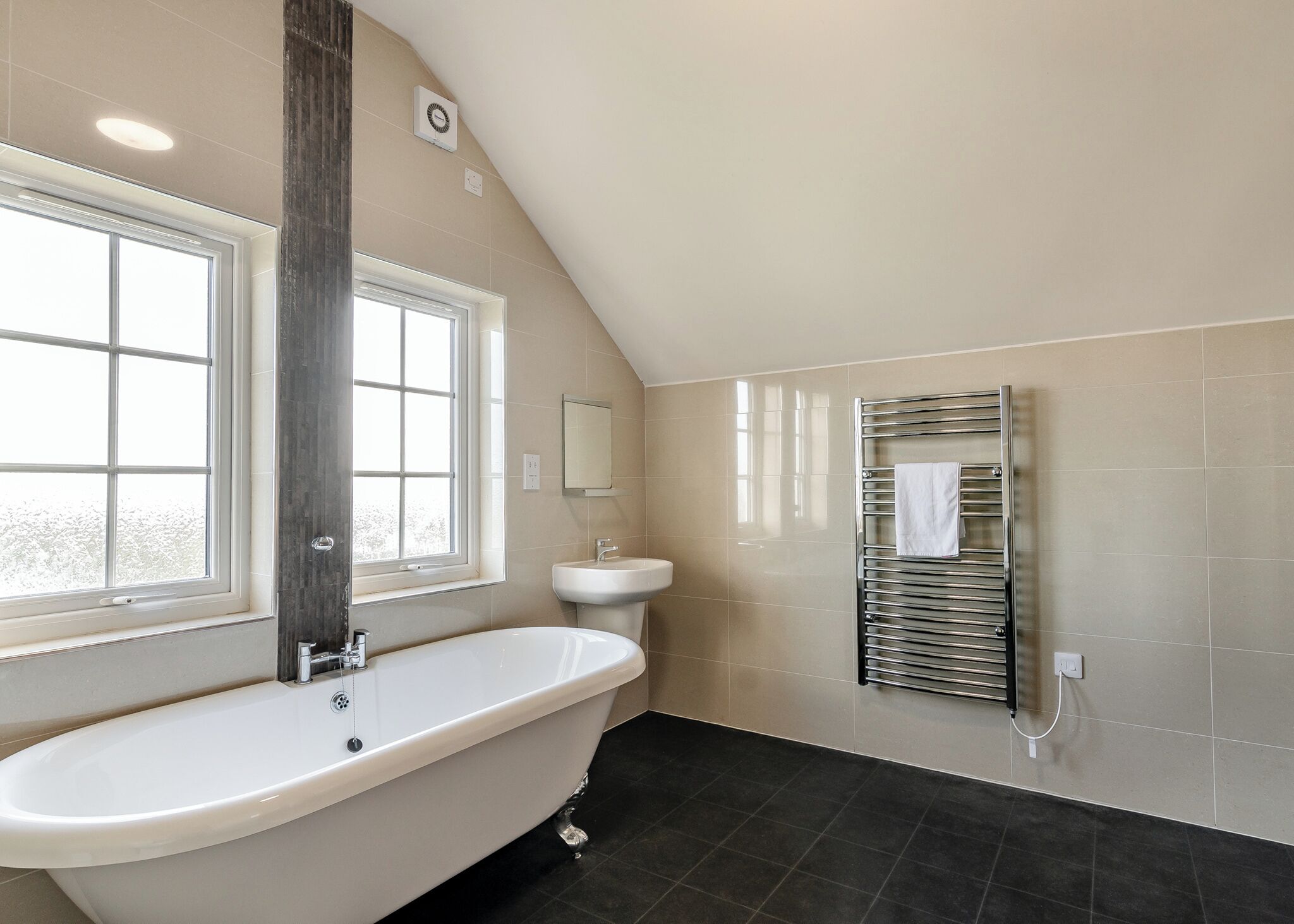 A bathroom with a freestanding bathtub, a window, a sink, and a towel rack.