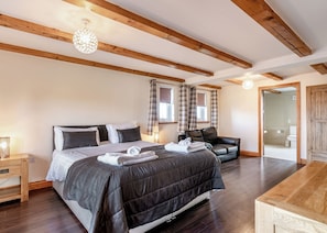 Ein Schlafzimmer mit einem Bett, Nachttischen, einer Holzbalkendecke und Blick ins Bad.