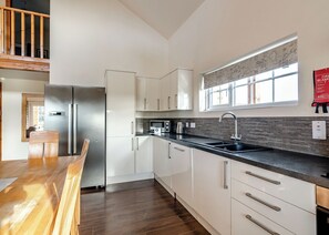 A modern kitchen with white cabinetry, a stainless steel refrigerator, a black countertop, and a window with a world map.