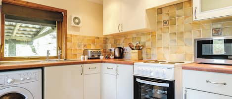 A compact kitchen with a washing machine, oven, microwave, and a window with a view.