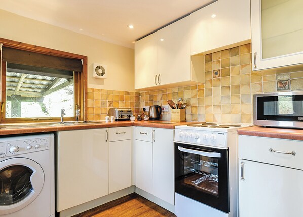 A compact kitchen with a washing machine, oven, microwave, and a window with a view.