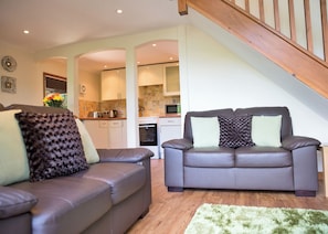A living room with two sofas, a staircase, and a kitchen in the background. - 2 bedroom accommodation in Waterrow, Wiveliscombe (Waterrow, Wiveliscombe)