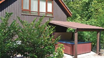 Une cabane en bois avec un jacuzzi, entourée de verdure.