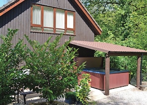 Une cabane en bois avec un jacuzzi, entourée de verdure.