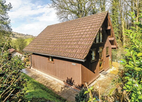 A wooden cabin with a sloped roof, surrounded by greenery and a clear sky. - 2 bedroom accommodation in Waterrow, Wiveliscombe (Waterrow, Wiveliscombe)