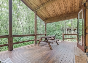 A wooden deck with a picnic table, surrounded by a forested area.