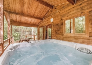 A wooden cabin with a hot tub, wooden deck, and large windows.