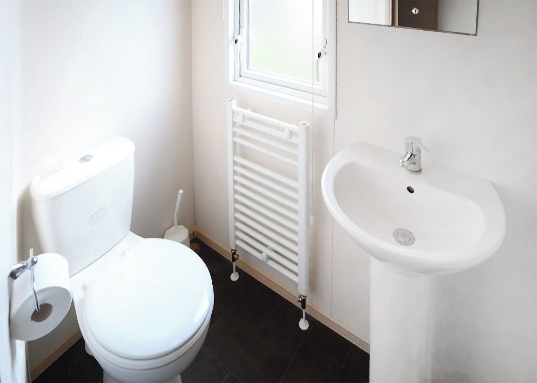 Ein kleines, sauberes Badezimmer mit Toilette, einem weißen Heizkörper und einem Waschbecken.