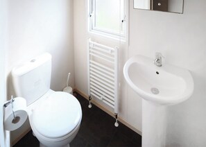 Une petite salle de bain propre, avec des toilettes, un radiateur blanc et un lavabo.