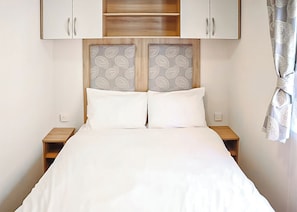 Ein Bett mit weißer Bettwäsche, zwei Nachttische, ein Holzkopfende mit gemusterten Feldern und ein Fenster mit Vorhang.