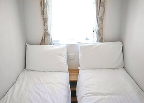 Habitación doble con dos camas individuales, ventana con cortinas y suelo de madera.