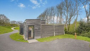 A small, modern building with a glass door, situated on a paved path with a grassy area and trees in the background. - Woodland View Retreat (Pet) (Lewes)