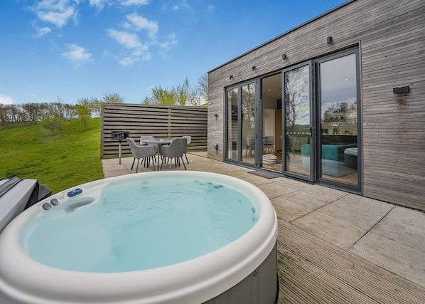 A hot tub with a patio, a dining area with chairs, and a modern building with large glass doors.