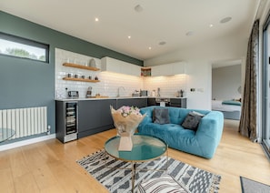 A modern kitchen with white tiles, a blue sofa, and a glass coffee table.