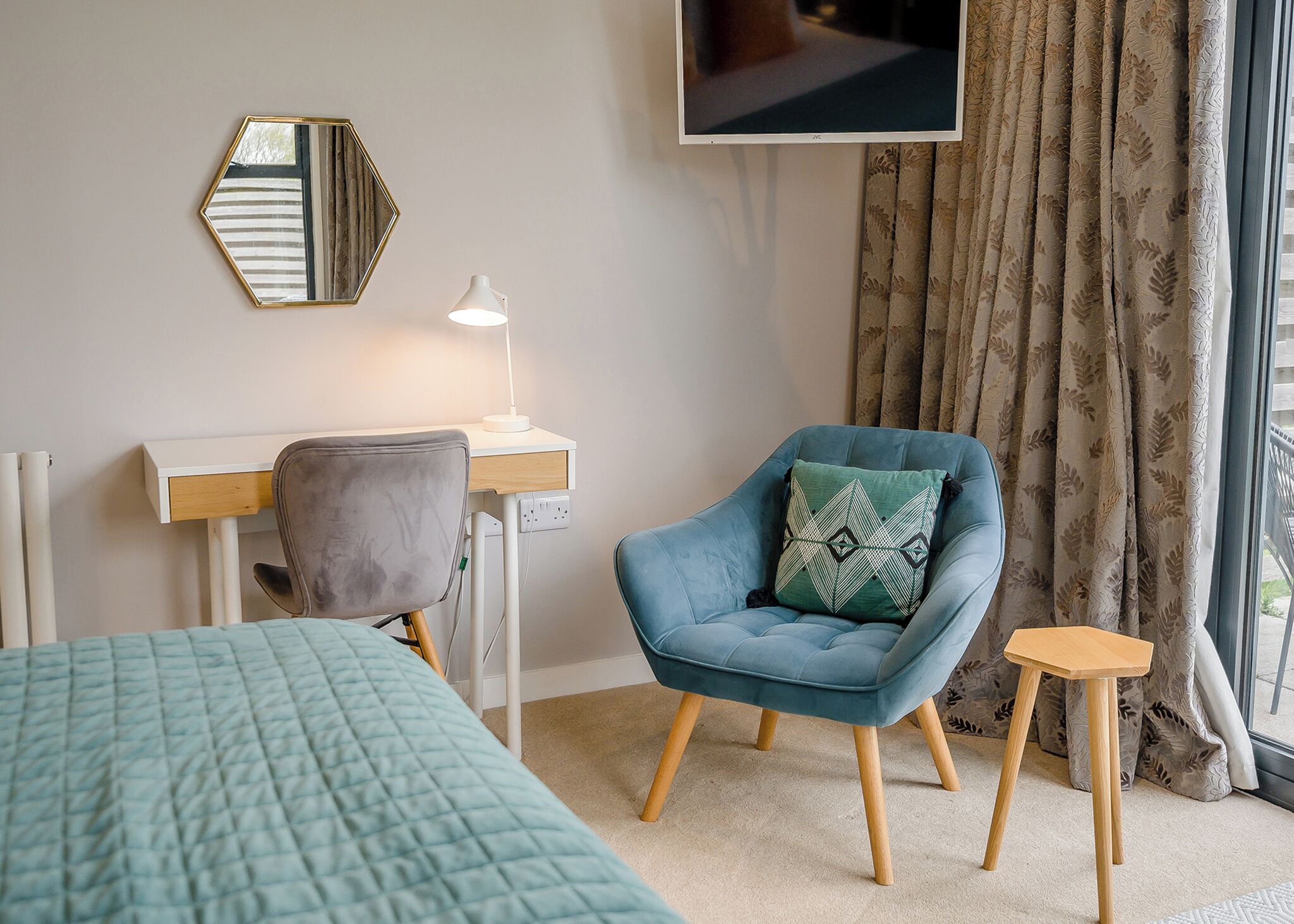 Une chambre avec un lit, un bureau et une chaise, une télévision et une fenêtre avec des rideaux.
