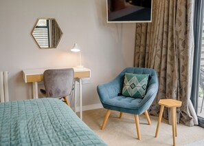 A room with a bed, a desk with a chair, a TV, and a window with curtains.