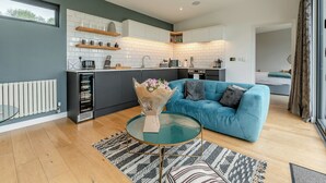 A modern kitchen with white tiles, a blue sofa, and a glass coffee table. - Woodland View Retreat (Pet) (Lewes)