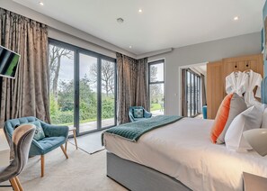 A modern bedroom with a large bed, two chairs, a TV, and a view of the outdoors.