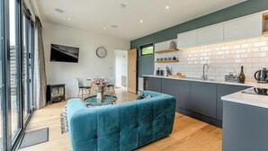 A modern kitchen with a central island, a dining area with a table and chairs, and a living space with a sofa. - Woodland View Retreat (Pet) (Lewes)