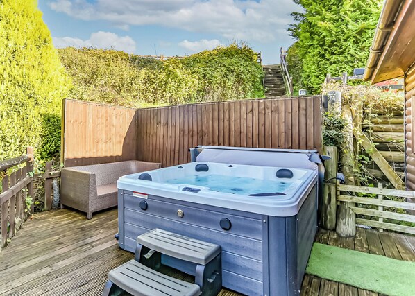 A hot tub on a wooden deck with a wooden fence and greenery in the background.