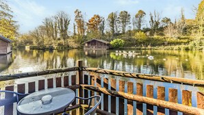 A lakeside view with a wooden dock, a table with chairs, and a building across the water. - Kingfisher Lakeside Lodge (Caerwys, Flintshire)