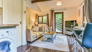 A compact living space with a washing machine, sofa, dining table, and a TV. - Kingfisher Lakeside Lodge (Caerwys, Flintshire)