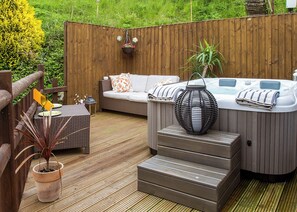 A wooden deck with a hot tub, a sofa, and a wicker table. - Kingfisher Lakeside Lodge (Caerwys, Flintshire)